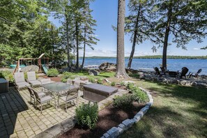 A patio area with outdoor furniture, a swing set, and a view of a lake. - Tranquil Waterfront, Modern, Dogs Welcome,Near Acadia National Park & Bar Harbor (Otis)