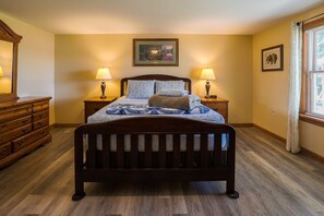 A bedroom with a wooden bed, two bedside lamps, a dresser, and a window with blinds. - Tranquil Waterfront, Modern, Dogs Welcome,Near Acadia National Park & Bar Harbor (Otis)