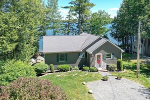 A single-story house with a red door, surrounded by a well-maintained lawn and various shrubs. - Tranquil Waterfront, Modern, Dogs Welcome,Near Acadia National Park & Bar Harbor (Otis)