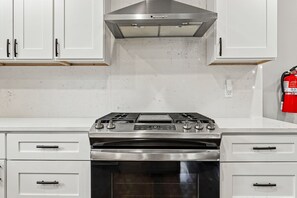 A kitchen with a stainless steel stove, white cabinets, and a fire extinguisher on the wall. - Evergreen Acres • Woodland Preserve • Private Pool (South Haven)