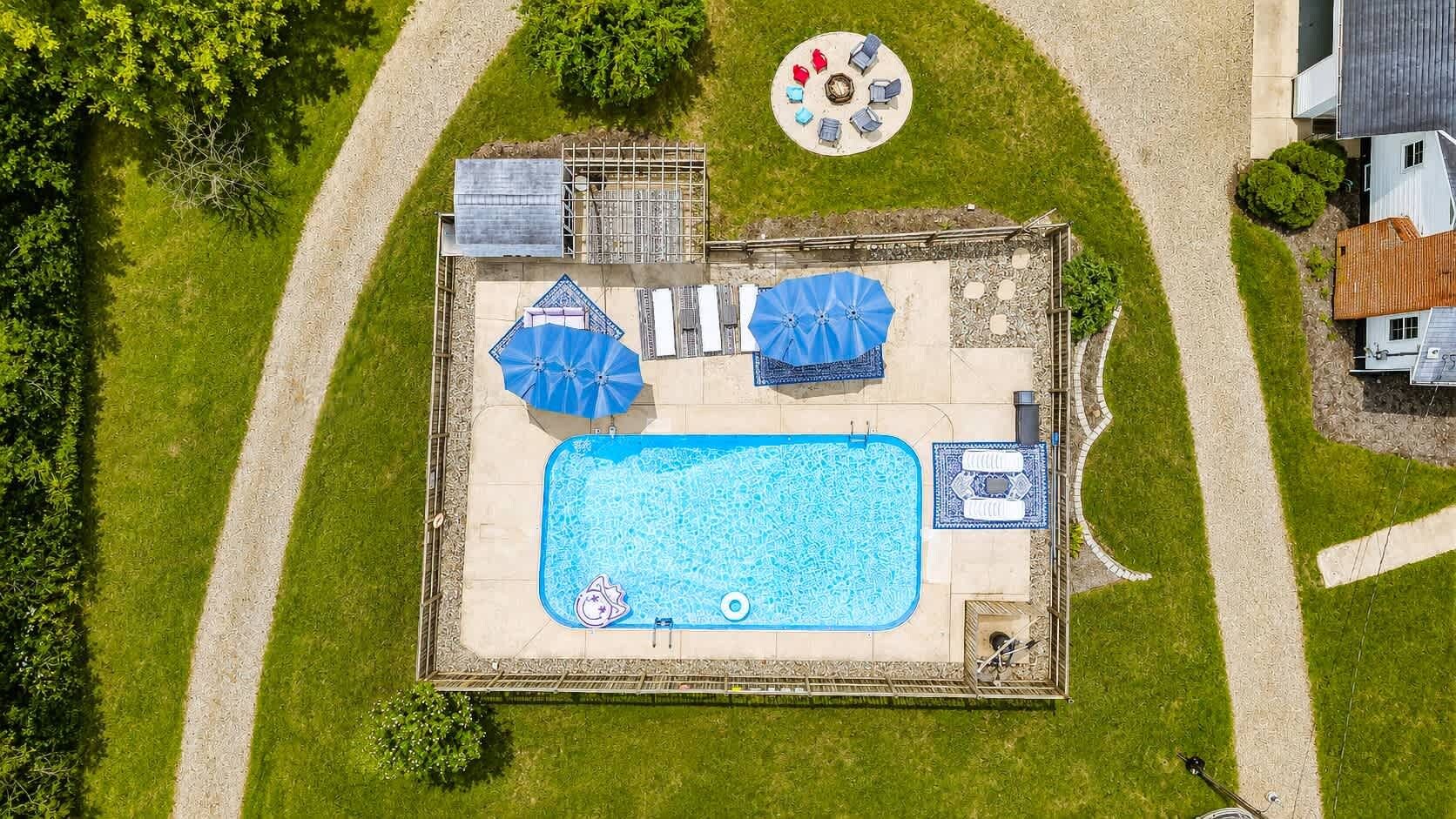 An aerial view of a backyard with a swimming pool, two umbrellas, a hot tub, and a circular seating area.