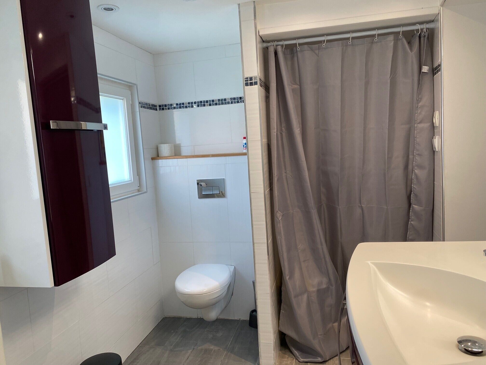 Een badkamer met toilet, douchegordijn, wastafel en raam.