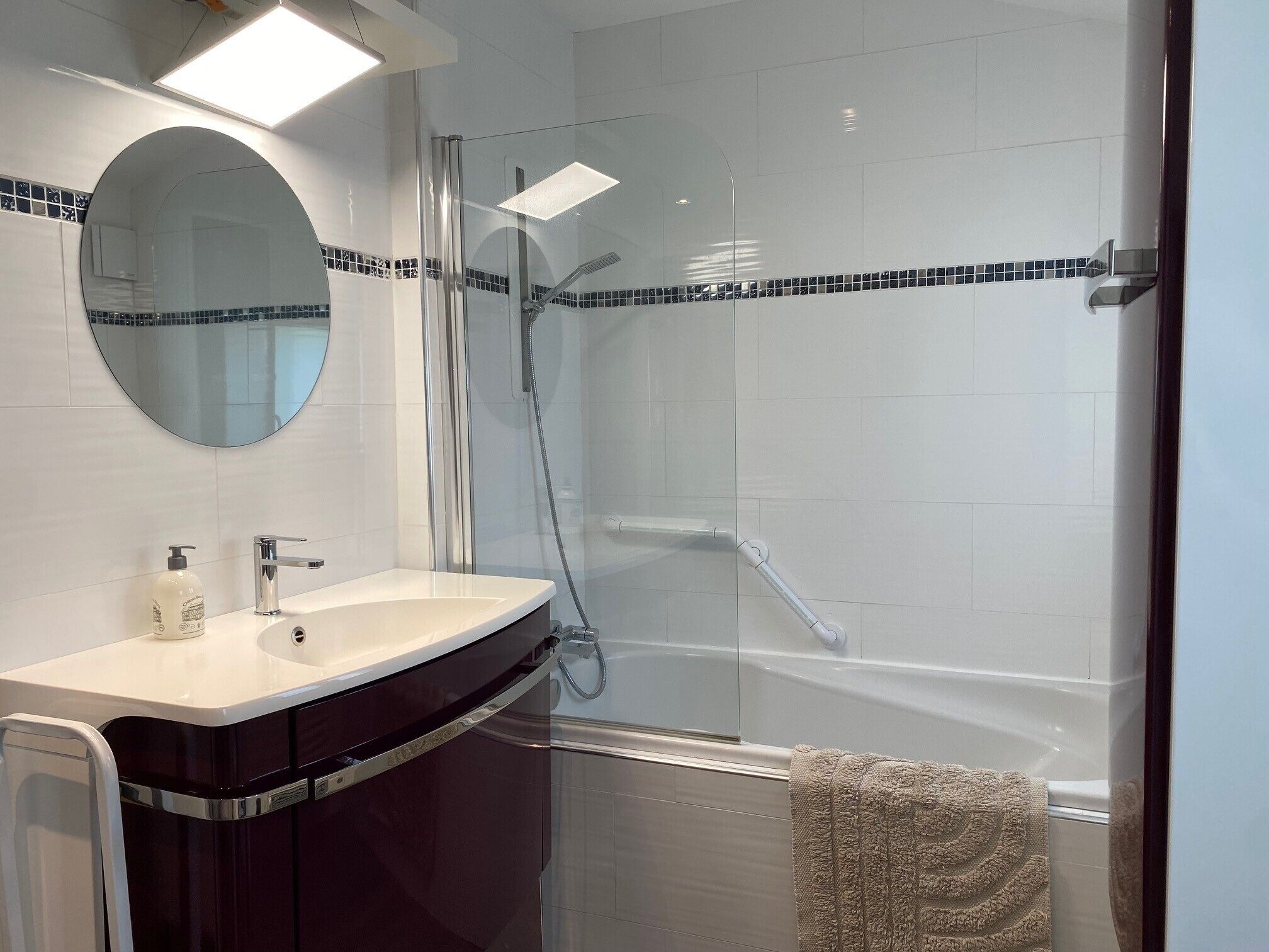 A modern bathroom with a glass-enclosed shower, a round mirror, and a white sink with a dark cabinet.