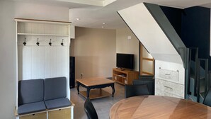 A modern living room with a sofa, a dining table, and a staircase. - Holiday Home "In the Heart of Nature" with Private Terrace, Shared Garden & Wi-Fi (Ambleteuse)