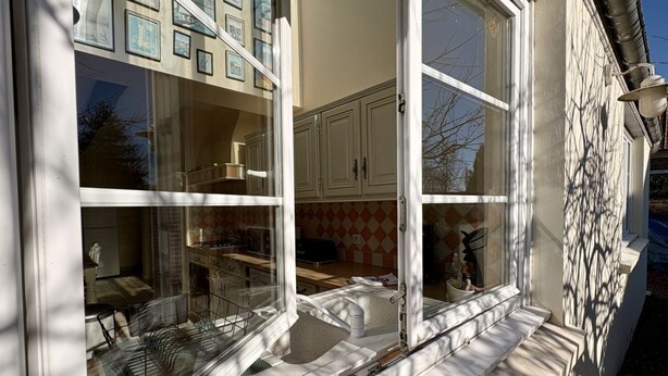 A room with a large window, a kitchen area with cabinets, and a dining table. - Charming renovated farmhouse - sleeps 6 (Boismont)