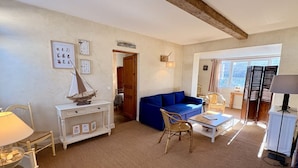 A living room with a blue sofa, a white cabinet, a wicker chair, a glass table, and a lamp. - Charming renovated farmhouse - sleeps 6 (Boismont)