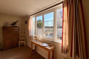 Ein Zimmer mit einem Holztisch, einem Stuhl, einem Fenster mit Vorhängen und einem Pfau auf einer Kommode.