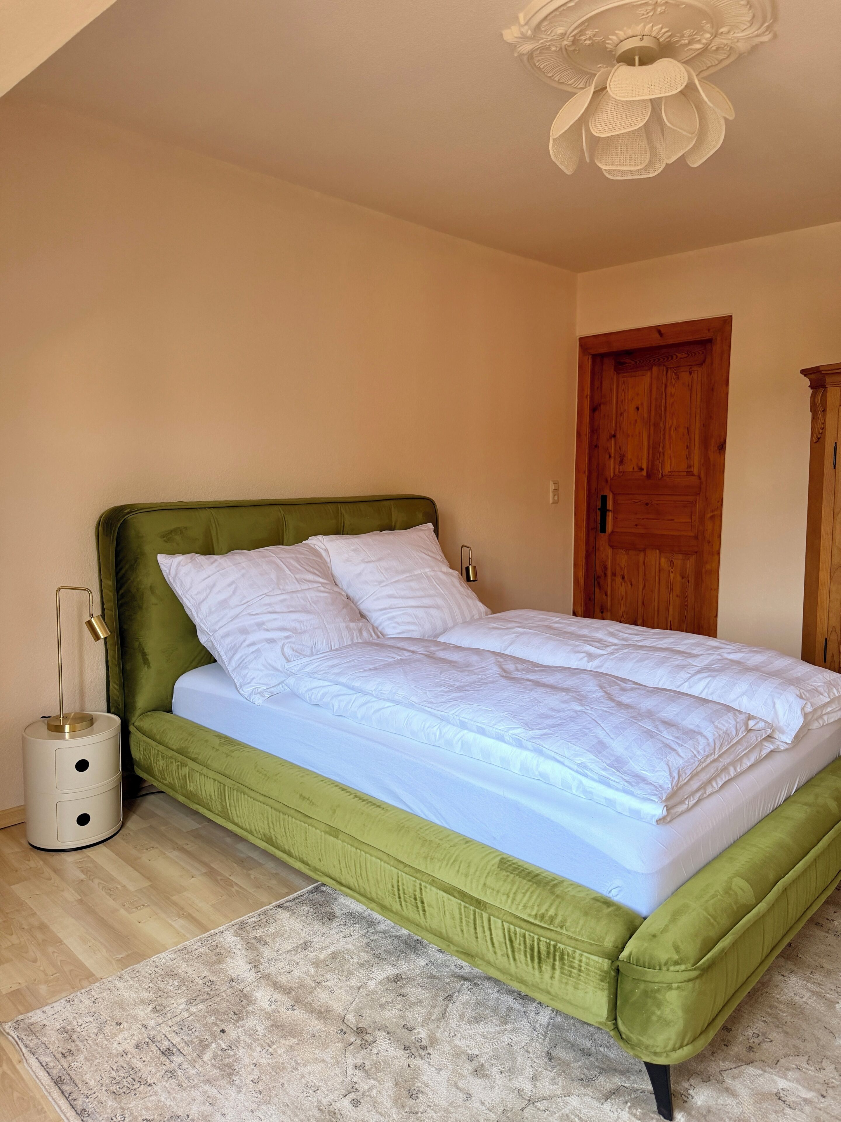 A room with a bed, a wooden door, a nightstand, and a lamp.