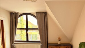 Une chambre à coucher avec un grand lit, une commode, une fenêtre avec des rideaux et un radiateur.