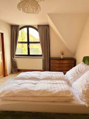 A bedroom with a large bed, a dresser, a window with curtains, and a radiator.