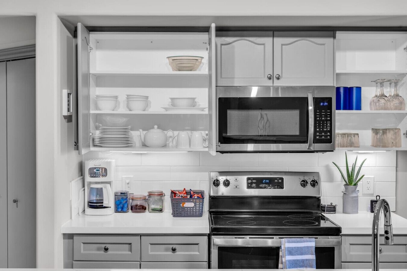 Una cucina moderna con mobili bianchi, forno a microonde integrato, macchina da caffè e fornello.