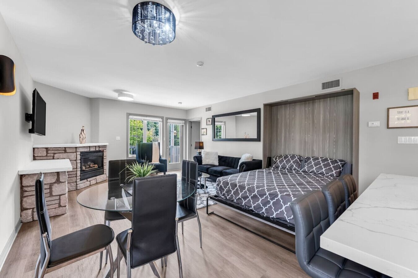 Una moderna camera d'hotel con camino in pietra, un tavolo da pranzo in vetro, un divano, un letto con biancheria a motivi decorativi e un grande specchio.