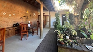 A rustic interior with brick walls, wooden furniture, and a variety of potted plants. - Suites in a cozy house with lots of greenery and a swimming pool. (Porto Seguro)
