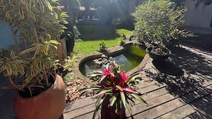 A garden with a pond, potted plants, and a wooden deck. - Suites in a cozy house with lots of greenery and a swimming pool. (Porto Seguro)