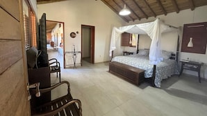 A bedroom with a bed under a canopy, a wooden bench, and a small table. - Suites in a cozy house with lots of greenery and a swimming pool. (Porto Seguro)
