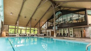 Una amplia piscina cubierta con techo alto y un balcón en el segundo piso con vistas a la piscina.