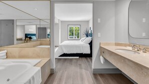 Una habitación de hotel moderna con un espejo grande, una bañera, una cama doble y un ventanal amplio.