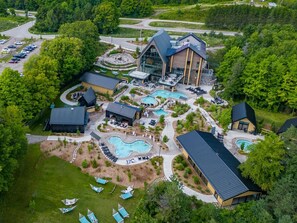 Une vue aérienne d’un complexe hôtelier doté de plusieurs piscines, d’espaces de détente en plein air et d’un grand bâtiment dont le toit se distingue par son architecture particulière.