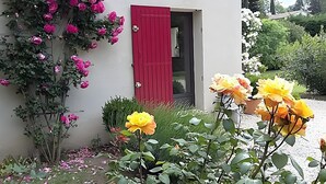 A building with a red shutter door, pink and yellow flowers, and a garden with various plants. - Holiday Home 'Chez Maté et Francis' with Private Terrace, Garden & Wi-Fi (Saint-Rémy-de-Provence)