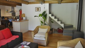 A living room with a sofa, a wicker chair, a dining area with a kitchen in the background, and a staircase leading to another level. - Holiday Home 'Chez Maté et Francis' with Private Terrace, Garden & Wi-Fi (Saint-Rémy-de-Provence)