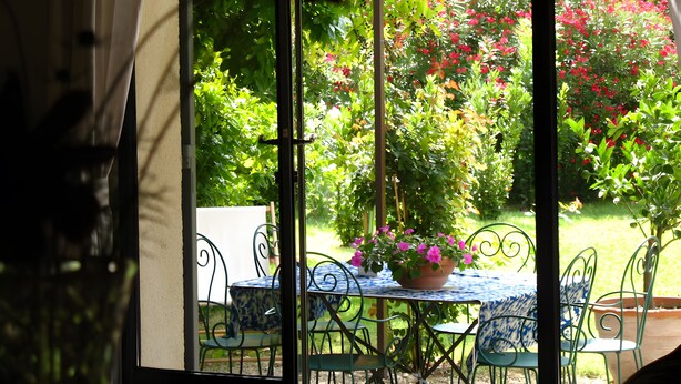 A covered patio with a table and chairs, a potted plant, and a view of a garden with various plants and flowers. - Holiday Home 'Chez Maté et Francis' with Private Terrace, Garden & Wi-Fi (Saint-Rémy-de-Provence)
