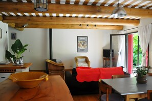 A cozy living room with a wooden ceiling, a dining table, a sofa with a red throw, and a television. - Holiday Home 'Chez Maté et Francis' with Private Terrace, Garden & Wi-Fi (Saint-Rémy-de-Provence)