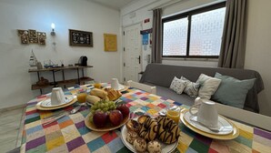 Ein Frühstückstisch mit Speisen und eine Couch in einem Zimmer mit Fenster und Tür.