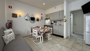 Ein kompakter Wohnraum mit Küchenzeile, einer Essecke mit Tisch und Stühlen, einer Couch und einem an der Wand montierten Feuerlöscher.