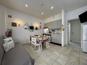 A compact living space with a kitchenette, a dining area with a table and chairs, a sofa, and a fire extinguisher on the wall.