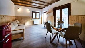 A spacious room with a wooden ceiling, a sofa, a dining table with chairs, and a window providing natural light. - Apt.Cristallo - `La Baita Civetta 1955` (Le Grazie)