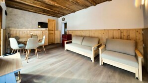A room with a wooden ceiling, a sofa, a dining table with chairs, and a red cabinet. - Apt.Cristallo - `La Baita Civetta 1955` (Le Grazie)