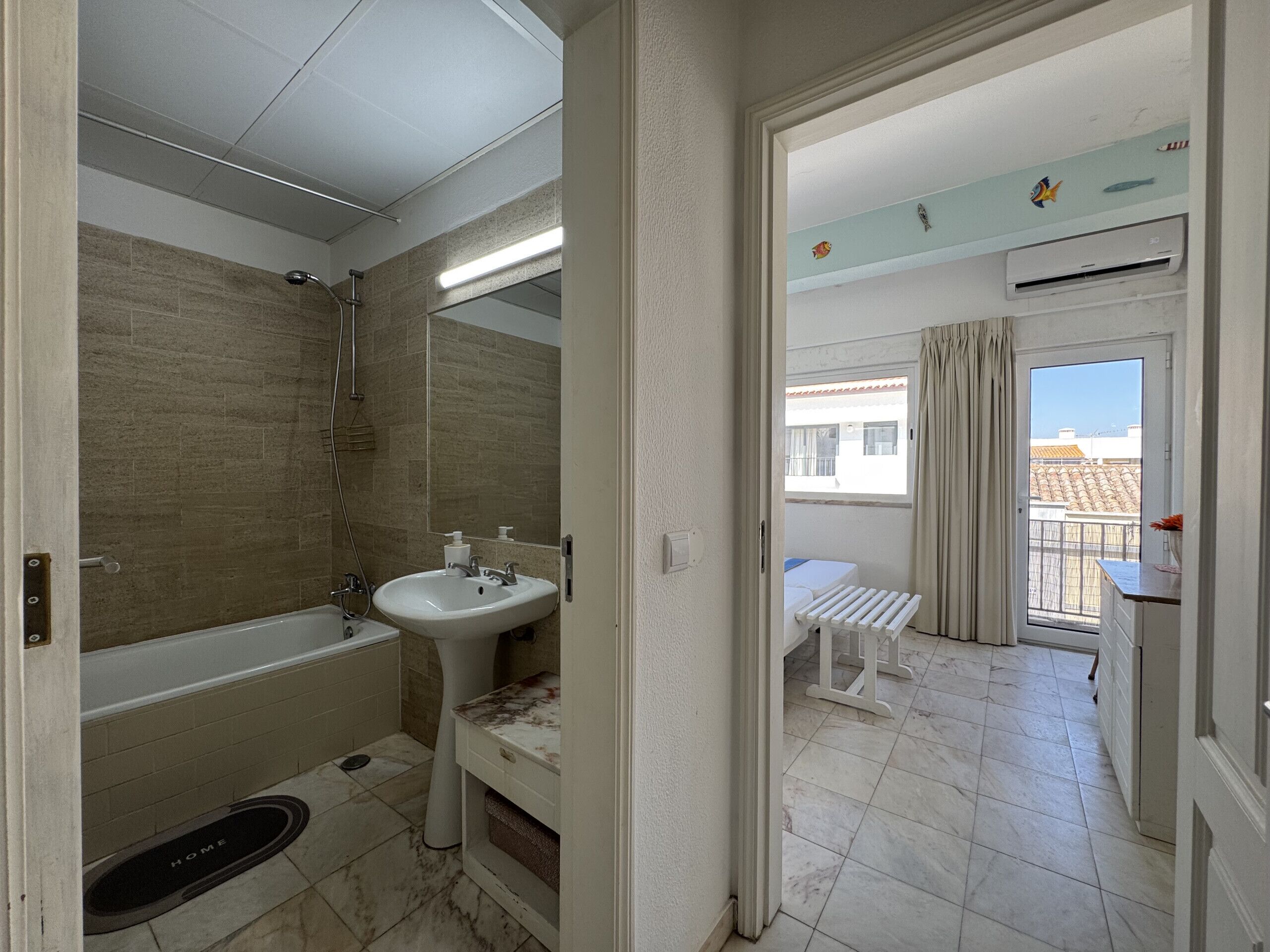A modern bathroom with a bathtub, sink, and shower. There is a balcony with a view of buildings.