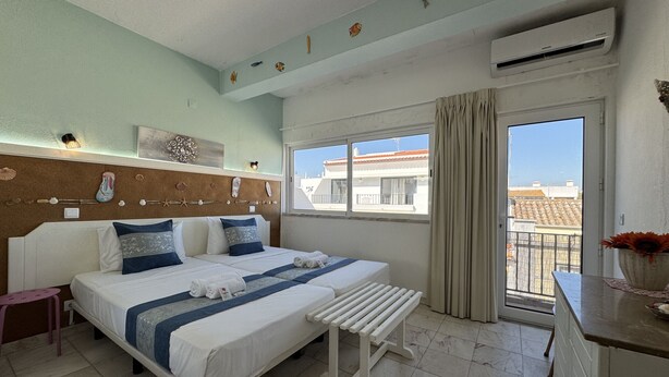 A hotel room with a bed, a bench, a window with a view, and a wall decorated with seashells and fish. - Cabanas DE Tavira Charming by Homing (Tavira)