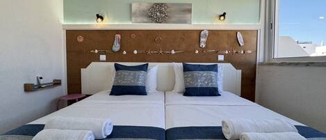 A double bed with two pillows, a headboard with decorative elements, and a window with a view of buildings.