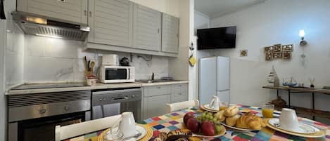 A kitchen with a microwave, stove, and sink. There is a table with breakfast items and a colorful tablecloth.