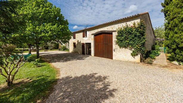 A stone building with a gravel driveway, a wooden door, and a small garden area.