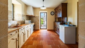 A kitchen with a tiled backsplash, a microwave, a sink, cabinets, and a door leading outside.