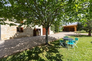 Ein Steinhaus mit überdachter Terrasse, einem Baum und Außenbestuhlung.