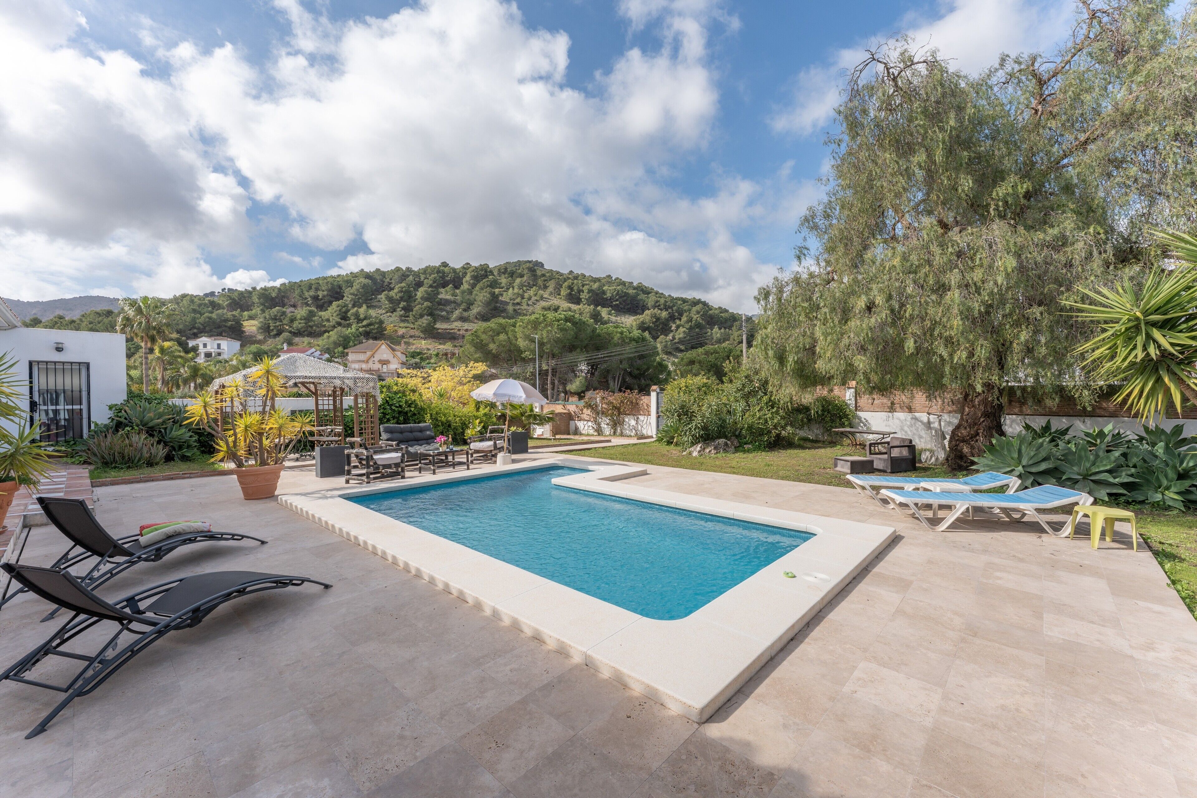 Une piscine rectangulaire, agrémentée de chaises longues et d’une pergola, dans un jardin aménagé.