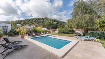Une piscine rectangulaire, agrémentée de chaises longues et d’une pergola, dans un jardin aménagé.
