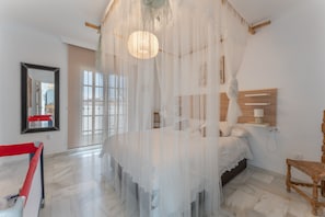 A bedroom with a canopy bed, a wooden headboard, a bedside table, and a chair.