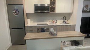 A modern kitchen with a built-in microwave, a refrigerator, and a wooden countertop. There are two white bar stools with metal bases.