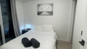 A modern hotel room with a large bed, a nightstand, a wall-mounted picture, and a sliding glass door leading to a balcony.