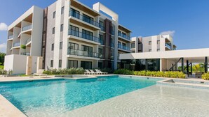 Ett modernt hotell med en swimmingpool, flera balkonger och ett vackert anlagt trädgårdsområde.