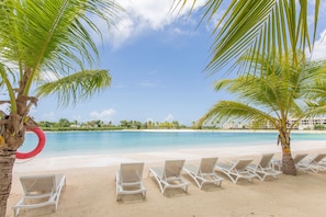 A beach with white lounge chairs and palm trees. - One-bedroom apartment in Vistacana, Punta Cana (Punta Cana)