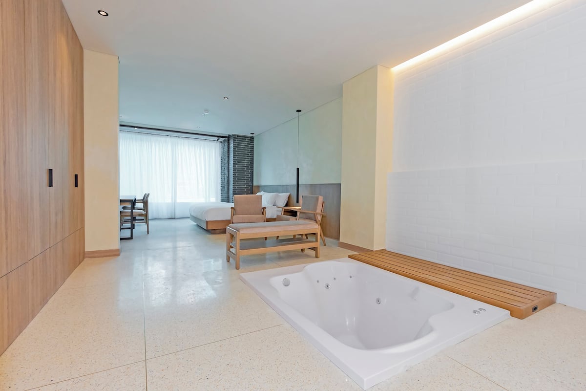 Un bagno moderno con una grande vasca, pavimento in legno e un'area salotto con sedie e una panca.