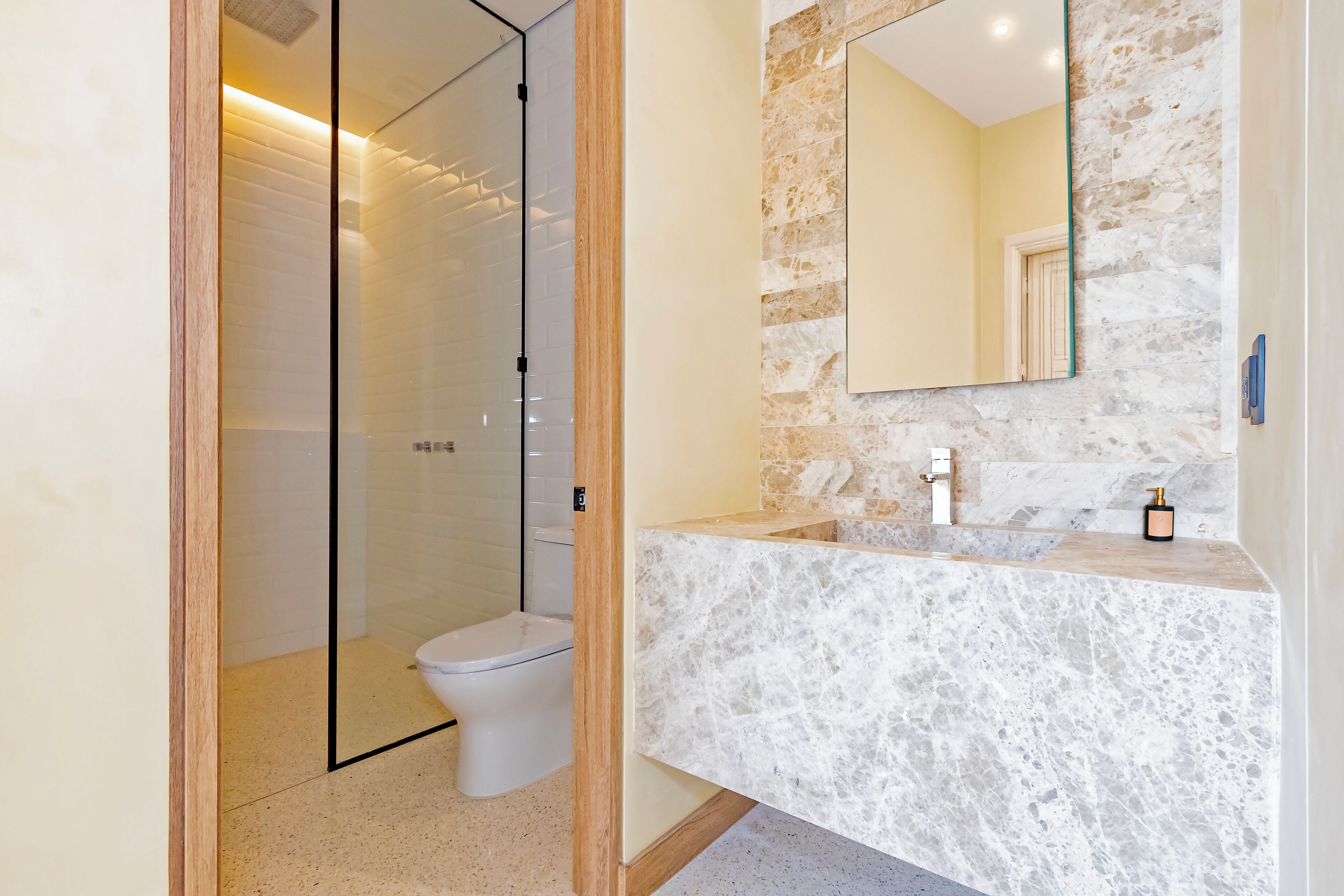 Une salle de bain moderne avec une douche à l’italienne en verre, un lavabo en marbre et un grand miroir.