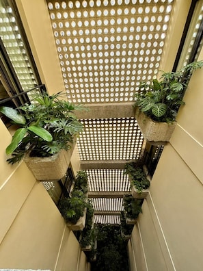 A narrow indoor corridor with a perforated ceiling, potted plants, and a tiled floor. - Hotel Iconik (Medellín)