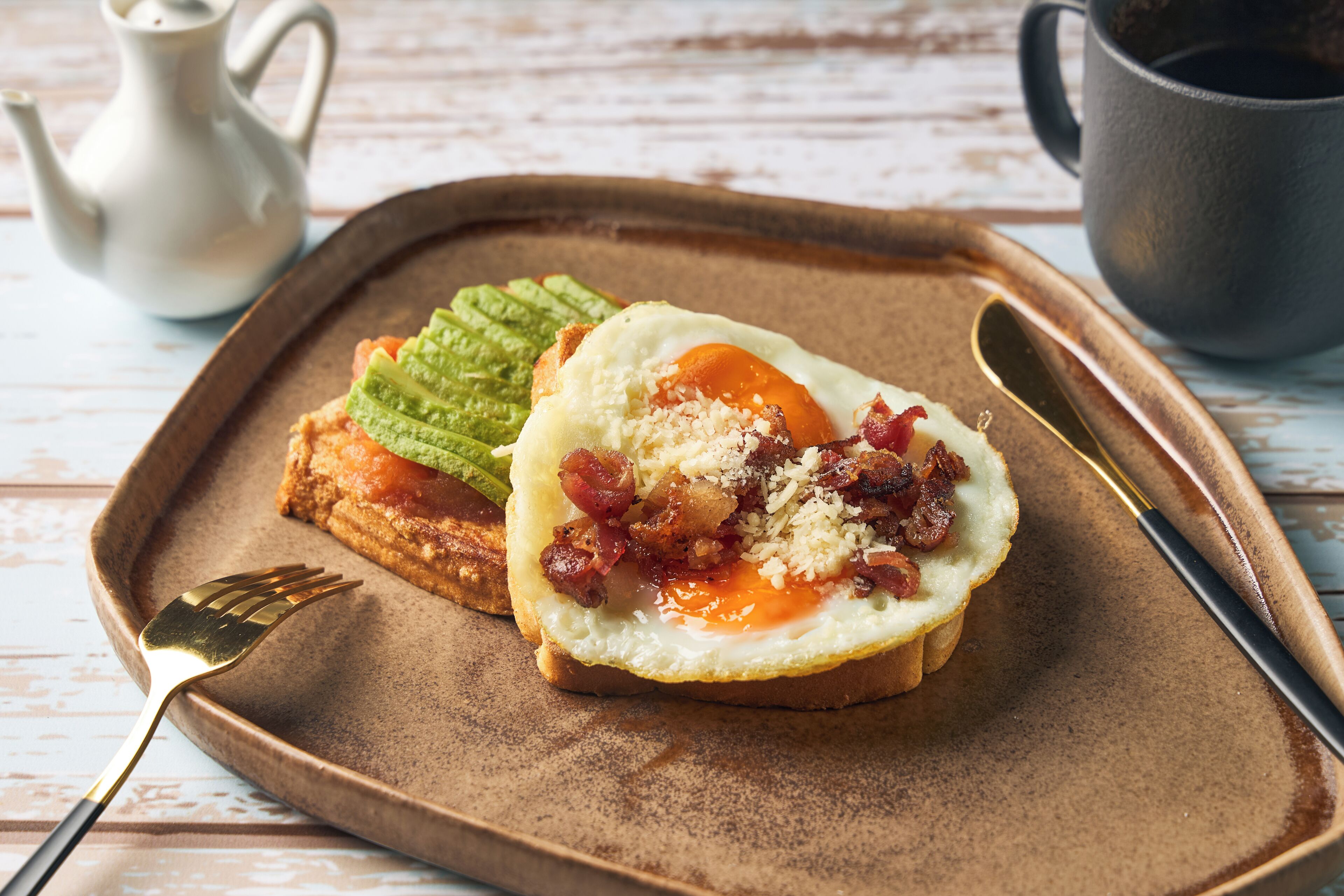A breakfast plate with toast, a fried egg, bacon, and a green sauce.