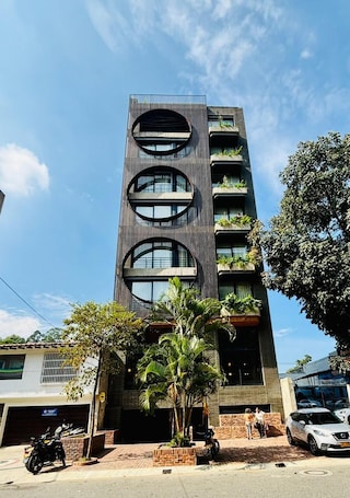 A modern building with a unique circular window design, multiple balconies with greenery, and a parking area with vehicles.. Hotel Iconik